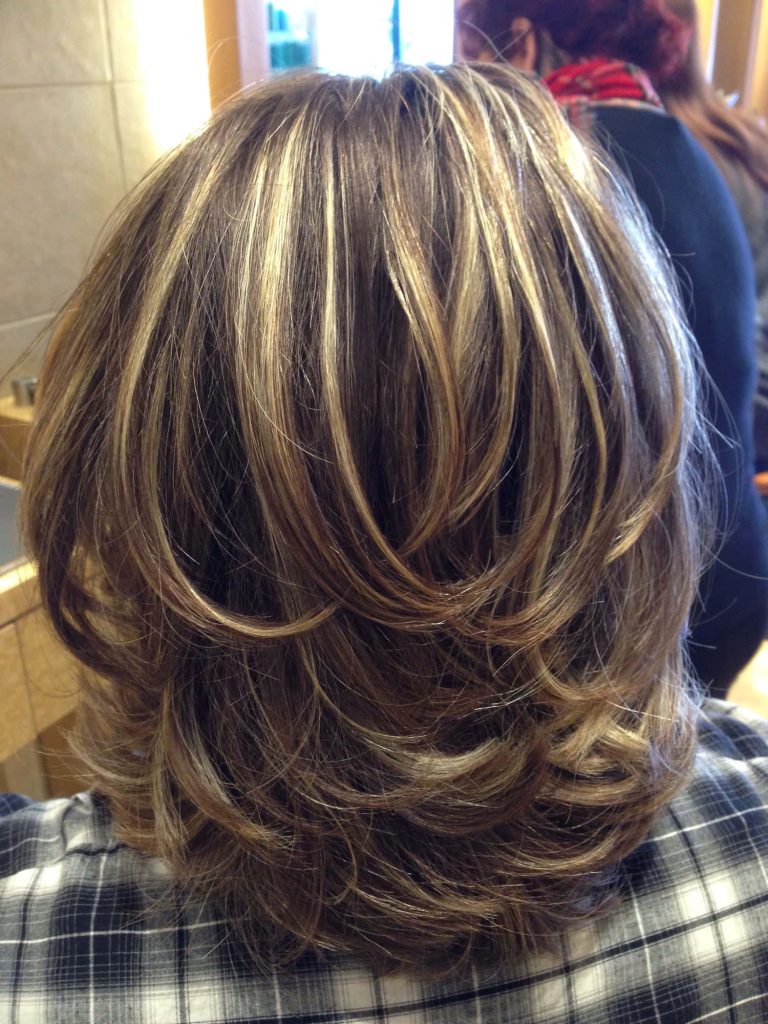 Back view of medium brunette layered haircut with soft blonde highlights in salon setting wallpaper