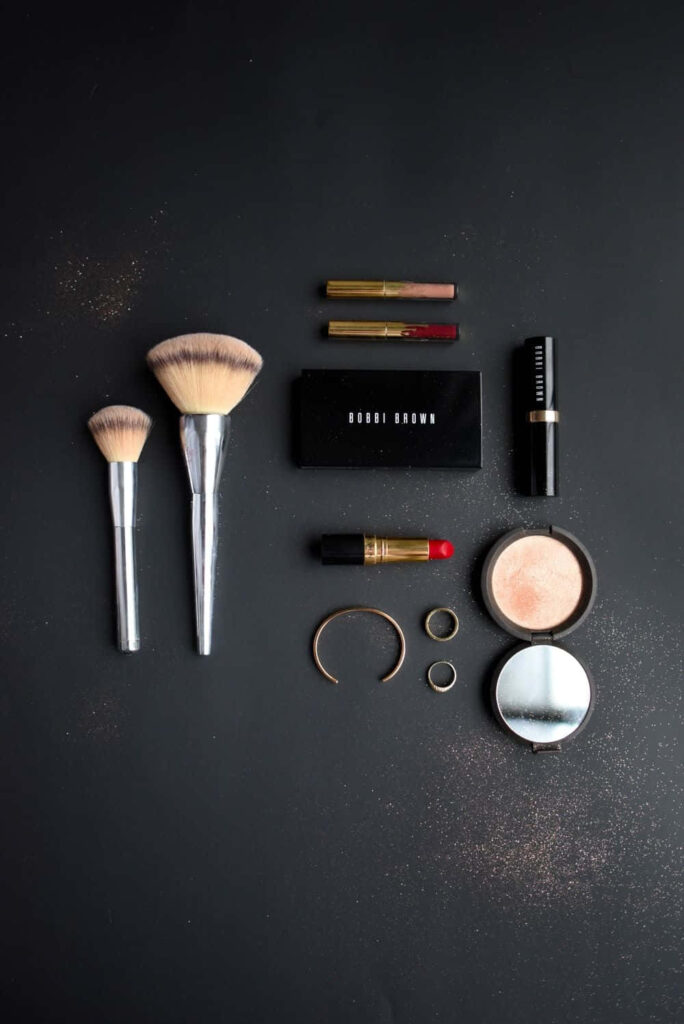 Flat lay of makeup essentials on black background with brushes lipsticks compact powder and gold accents Wallpaper
