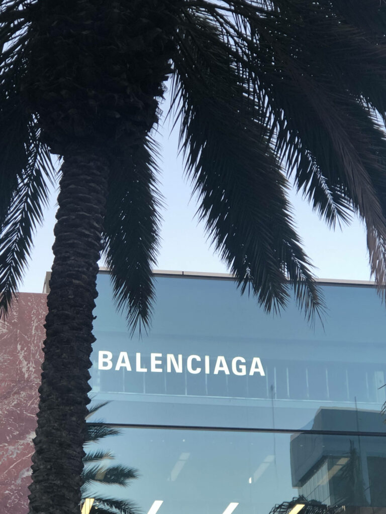 Stylish palm tree outside modern glass building with bold white Balenciaga logo office background Wallpaper