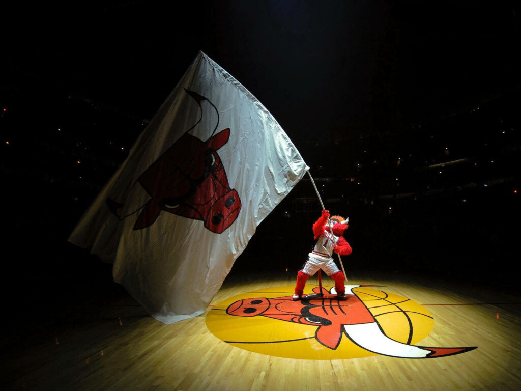 Chicago Bulls mascot waving flag with bull logo at center court in vibrant basketball arena Wallpaper