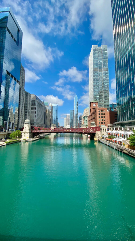 Chicago Riverwalk with iconic glass skyscrapers reflected in turquoise water under blue sky Wallpaper