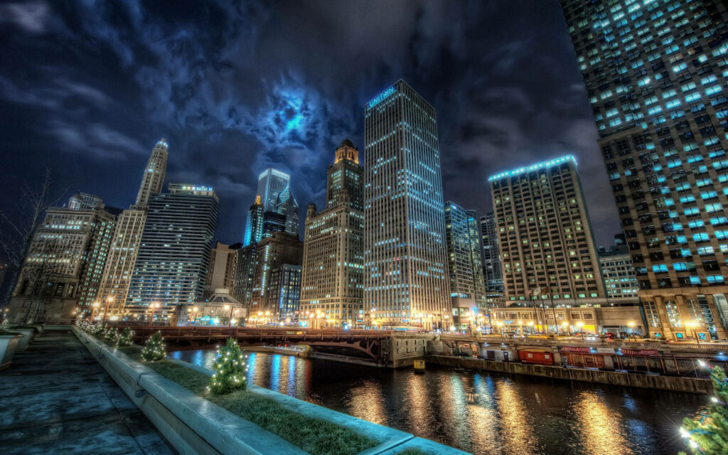 Chicago skyline at night glowing skyscrapers reflecting on river under dramatic moody sky Wallpaper