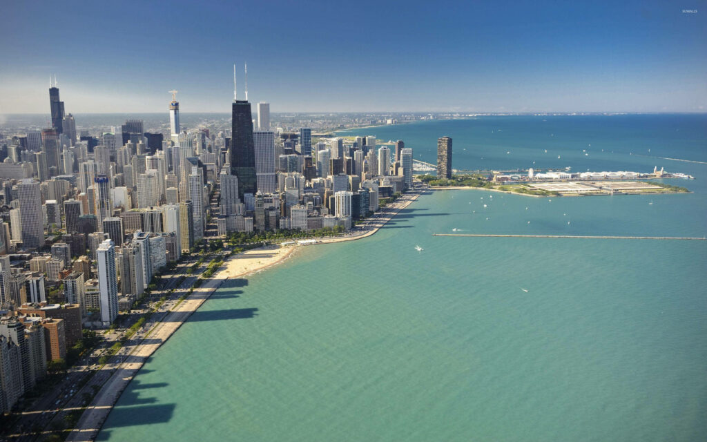Aerial view of Chicago skyline over turquoise Lake Michigan with beaches sailboats under blue sky Wallpaper