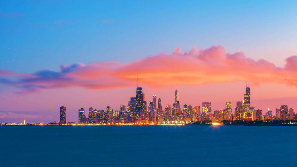 Chicago skyline at sunset with illuminated skyscrapers reflecting on Lake Michigan in vibrant colors Wallpaper