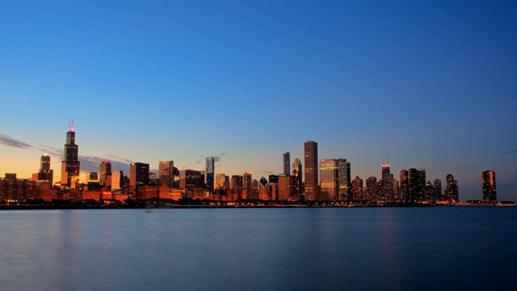 Chicago skyline at sunset with glowing skyscrapers reflecting golden hues on calm water wallpaper