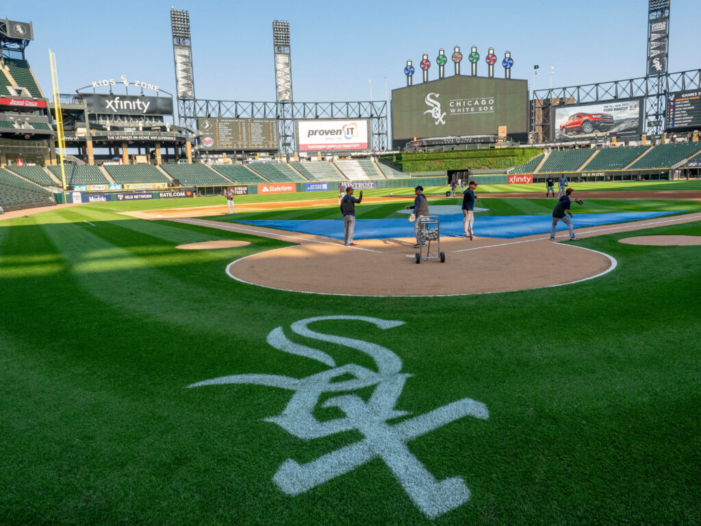 Chicago White Sox logo on home plate with lush infield and stadium seating under blue sky Wallpaper