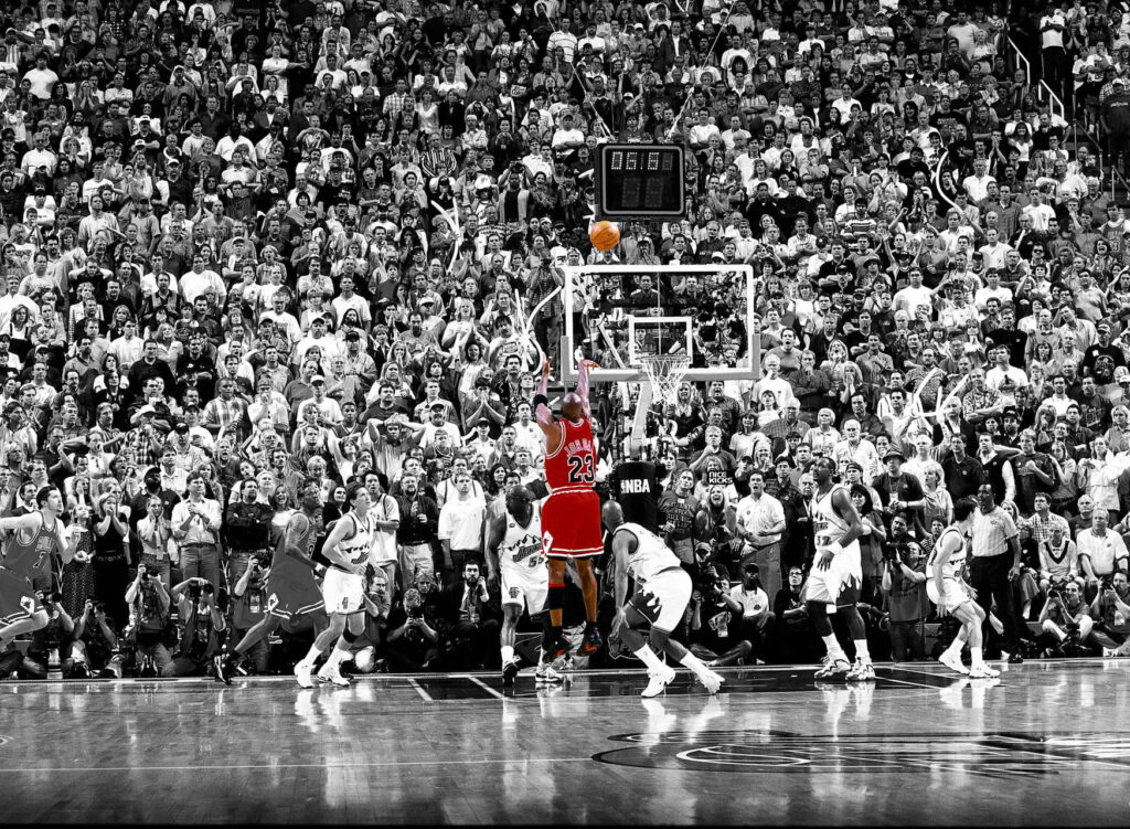 Michael Jordan in red Bulls jersey soaring for legendary jump shot with Utah Jazz players background Wallpaper