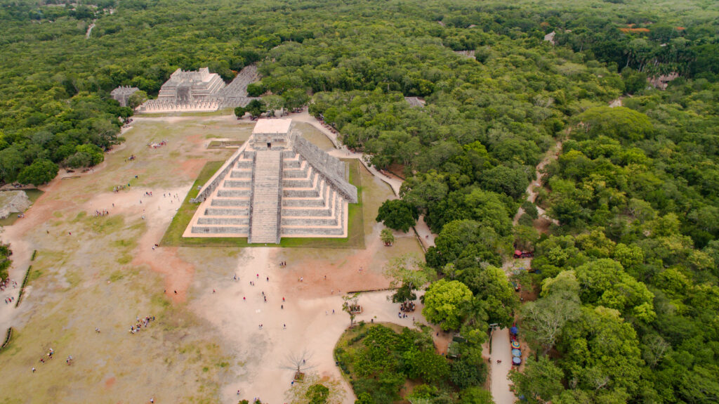 Aerial view of Chichén Itzá pyramid surrounded by lush green Mayan jungle in soft earthy tones Wallpaper