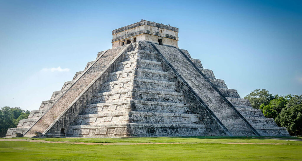 Side view of Chichén Itzá pyramid with blue sky and green grass ancient Mayan architecture wallpaper