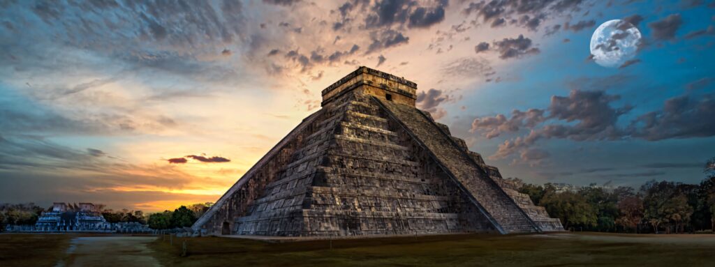 Chichén Itzá pyramid at sunset with moon rising and dramatic clouds in golden blue tones Wallpaper