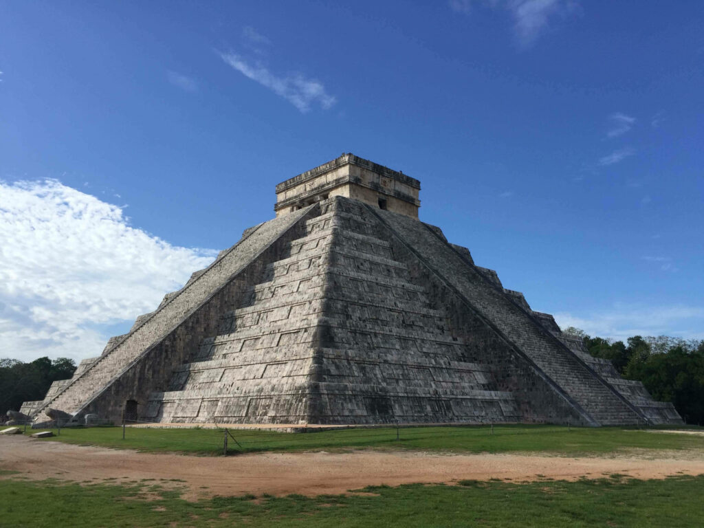 Chichén Itzá pyramid under blue sky with detailed stone steps and lush green surroundings wallpaper