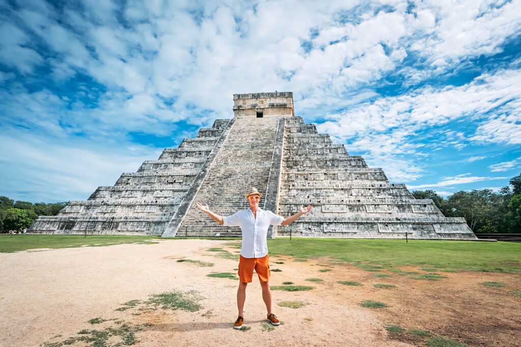 Tourist enjoying Chichén Itzá pyramid under blue sky with clouds and lush green surroundings wallpaper