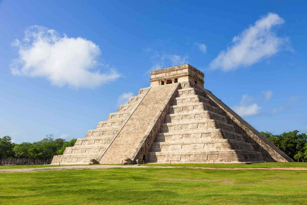 Chichén Itzá pyramid under blue sky with clouds lush green grounds ancient Mayan site wallpaper