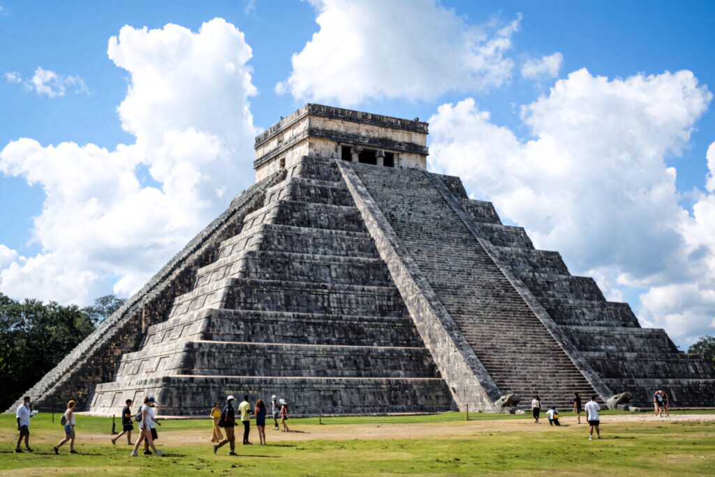 Chichén Itzá pyramid with sharp stone steps under blue sky and clouds surrounded by greenery Wallpaper