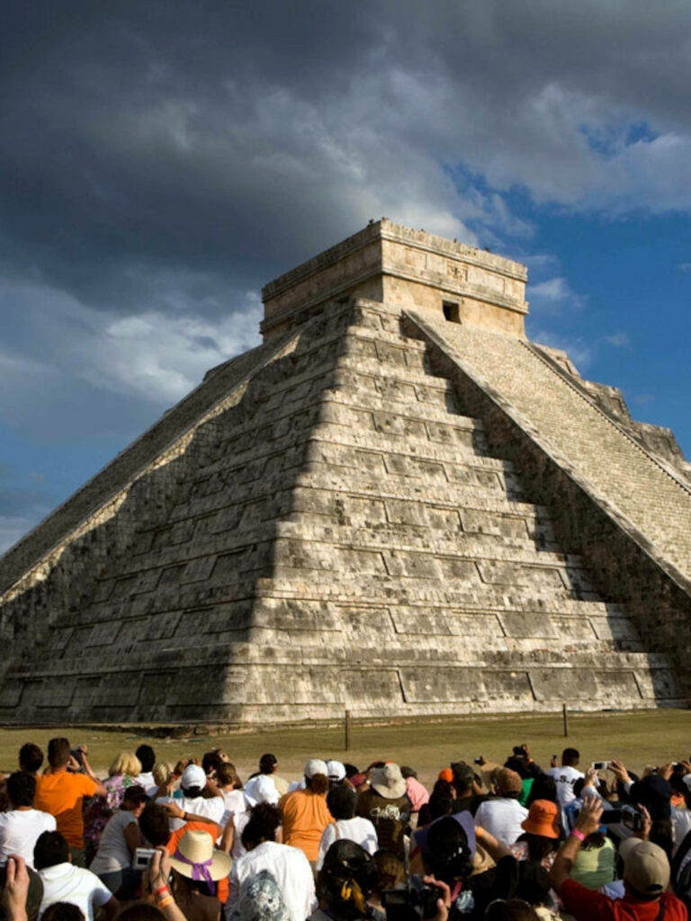 Tourists exploring Chichen Itza Pyramid under dramatic sky showcasing ancient Mayan architecture Wallpaper