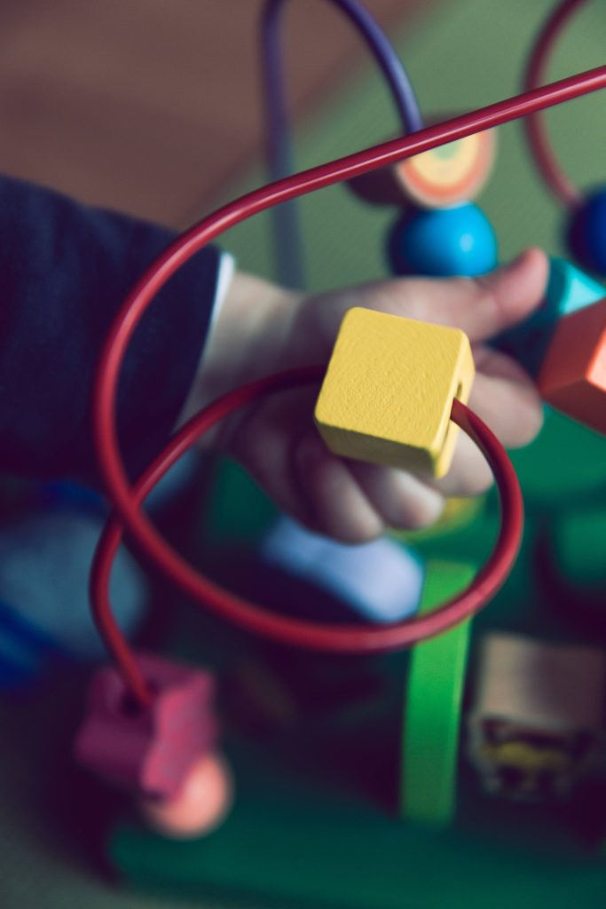 Child's hand sliding yellow block on colorful wooden wire bead maze toy early learning play Wallpaper