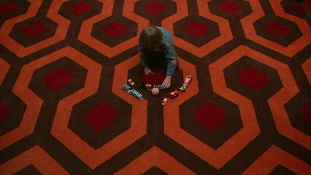 Child Playing with Toy Cars on Vibrant Carpet Inspired by The Shining Wallpaper