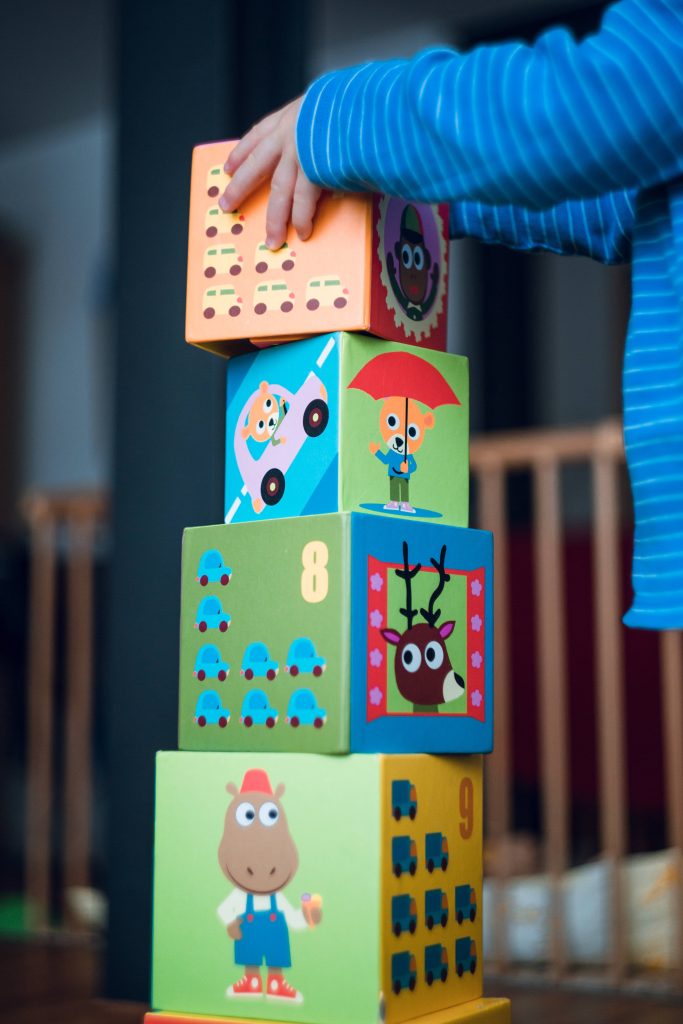 Child in blue striped shirt stacking colorful educational blocks with animals cars and numbers indoors Wallpaper