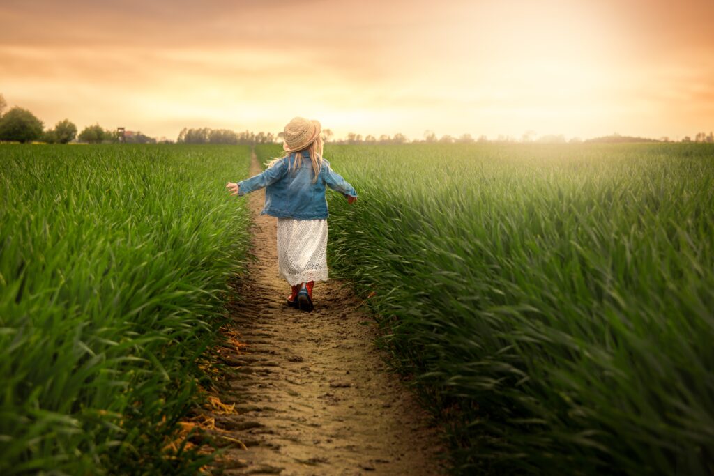 Young child walking on narrow path through lush green grass in sunlit golden field at sunset Wallpaper