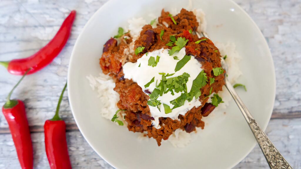 Chili con carne over white rice with sour cream cilantro and red chili peppers on wood background Wallpaper