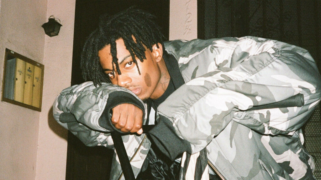 Confident Playboi Carti in camo jacket poses with direct gaze Wallpaper
