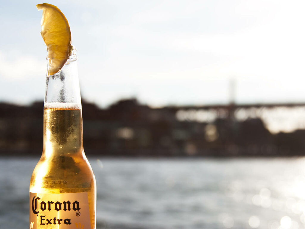 Chilled Corona Extra bottle with lemon by peaceful sunlit riverside for relaxing escape wallpaper