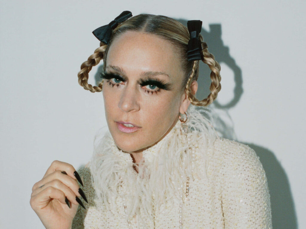 Chloë Sevigny portrait with dramatic makeup braided hair black bows feather outfit soft background Wallpaper