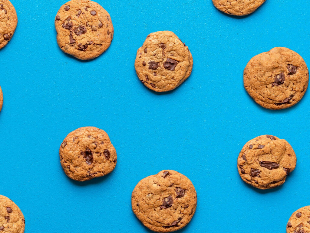 Chocolate chip cookies scattered on vibrant blue background tasty food wallpaper pattern