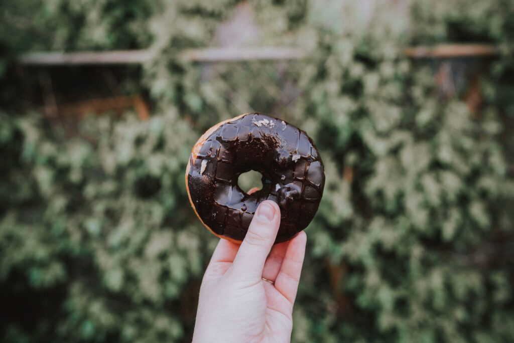 Chocolate-Covered Donut Handheld Against Leafy Green Wallpaper