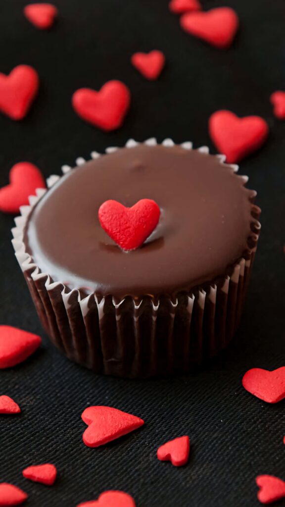 Chocolate cupcake with red heart topping and scattered hearts on dark background wallpaper