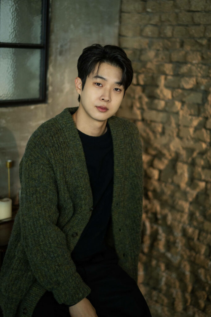 Choi Woo-shik in cozy green cardigan and black shirt with rustic brick background wallpaper