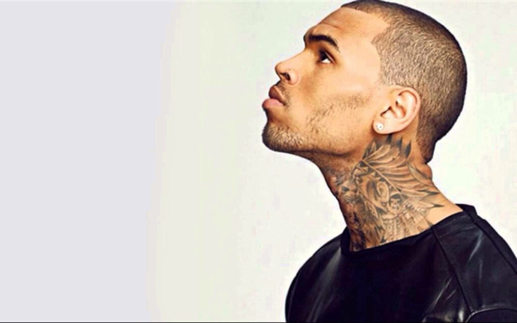 Chris Brown side profile with detailed neck tattoos and sharp features on light background wallpaper