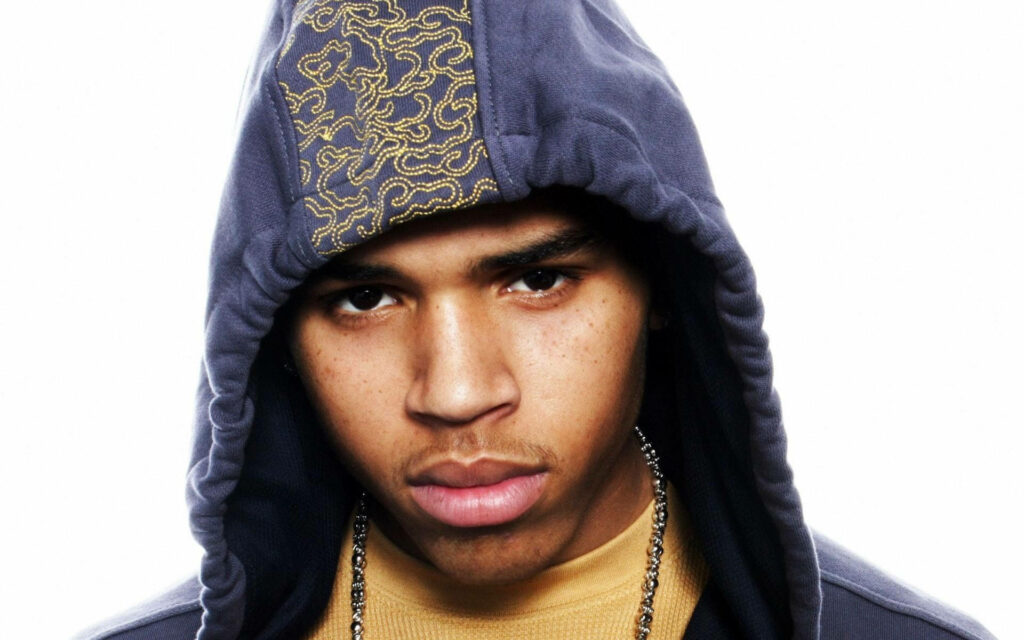 Chris Brown wearing stylish hoodie jacket with focused expression on clean wallpaper background