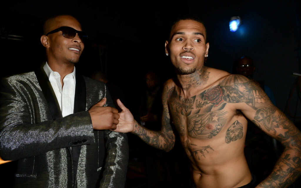 Chris Brown shirtless with tattoos and T.I. in suit backstage candid moment dimly lit background Wallpaper