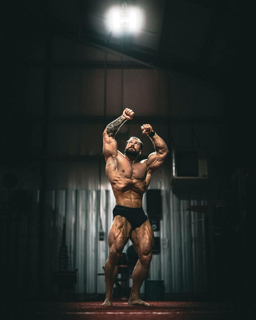 Chris Bumstead bodybuilding vacuum pose highlighting defined muscles in dramatic gym lighting Wallpaper