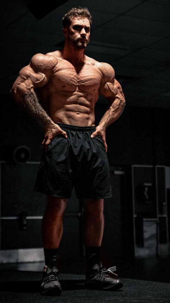 Chris Bumstead front lat spread pose muscular physique dramatic lighting dark gym wallpaper
