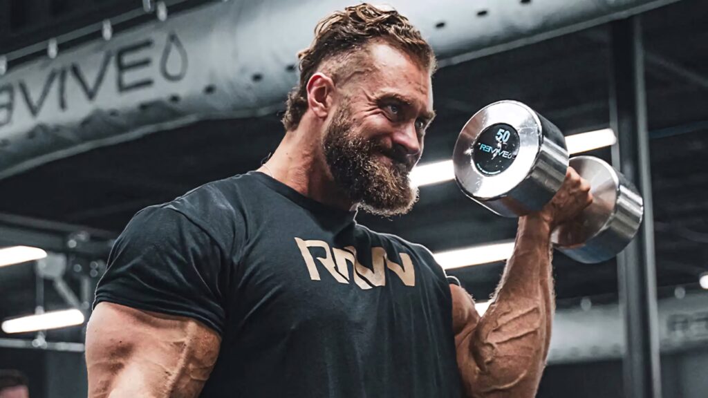 Chris Bumstead lifting heavy dumbbell in gym showing muscular physique and intense focus Wallpaper
