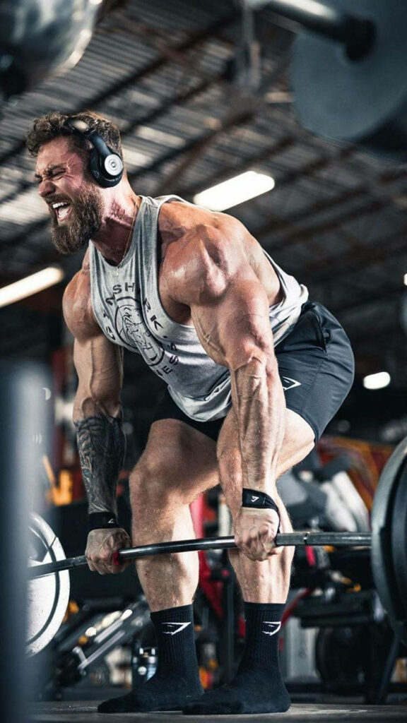 Chris Bumstead lifting heavy weights in industrial gym showing muscular physique and tattoos Wallpaper