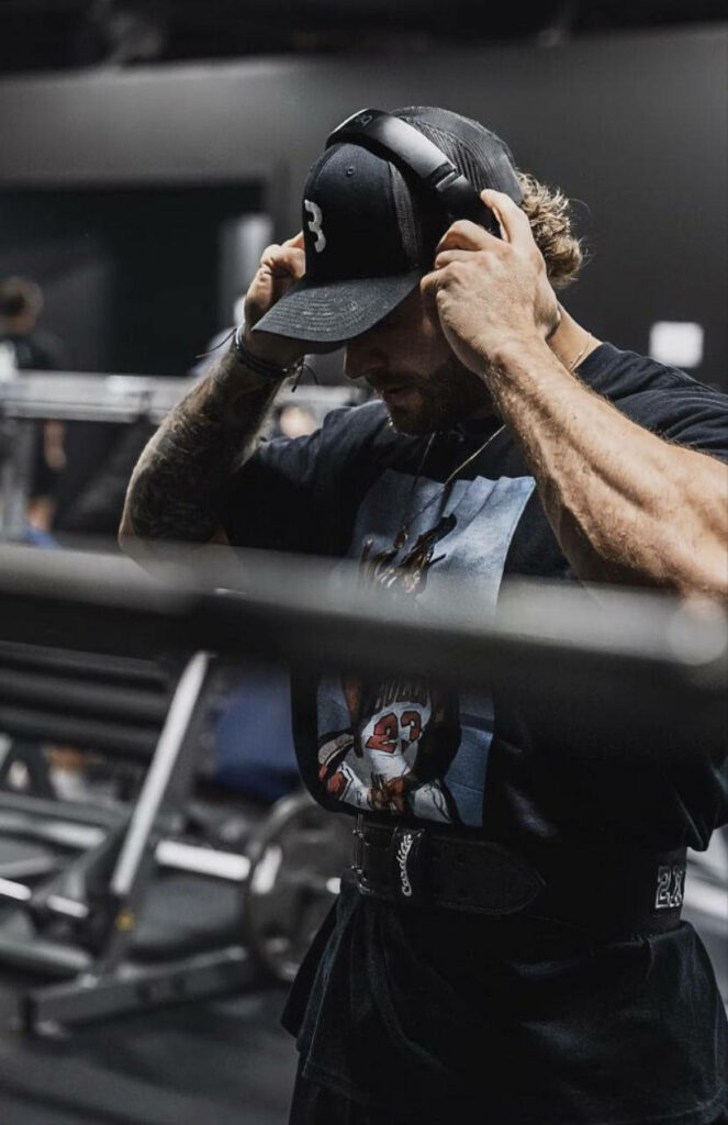 Chris Bumstead adjusting headphones in gym showing muscular physique and focused workout intensity Wallpaper