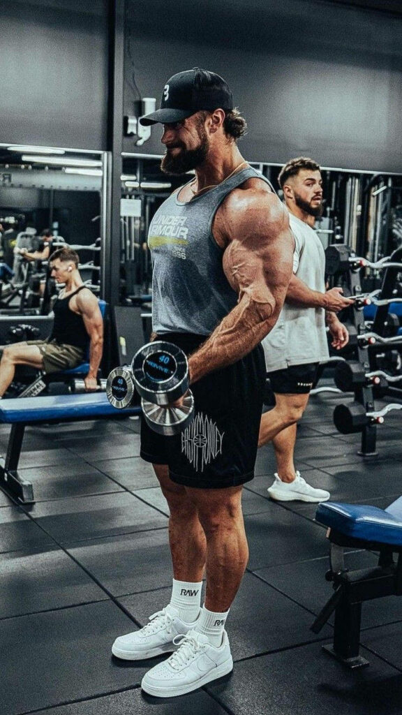 Chris Bumstead lifting dumbbells in gym side profile showing muscular physique and focus Wallpaper
