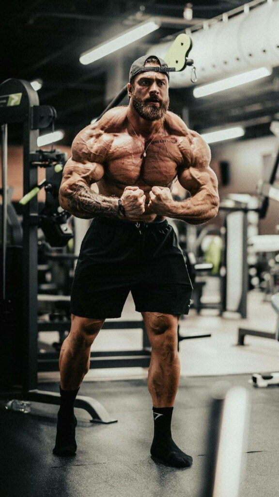 Chris Bumstead striking most muscular pose in gym highlighting defined muscles and vascularity Wallpaper