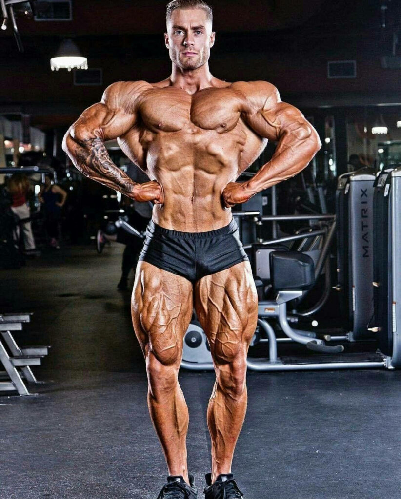 Chris Bumstead rear lat spread pose showing broad shoulders defined back and muscular legs gym Wallpaper