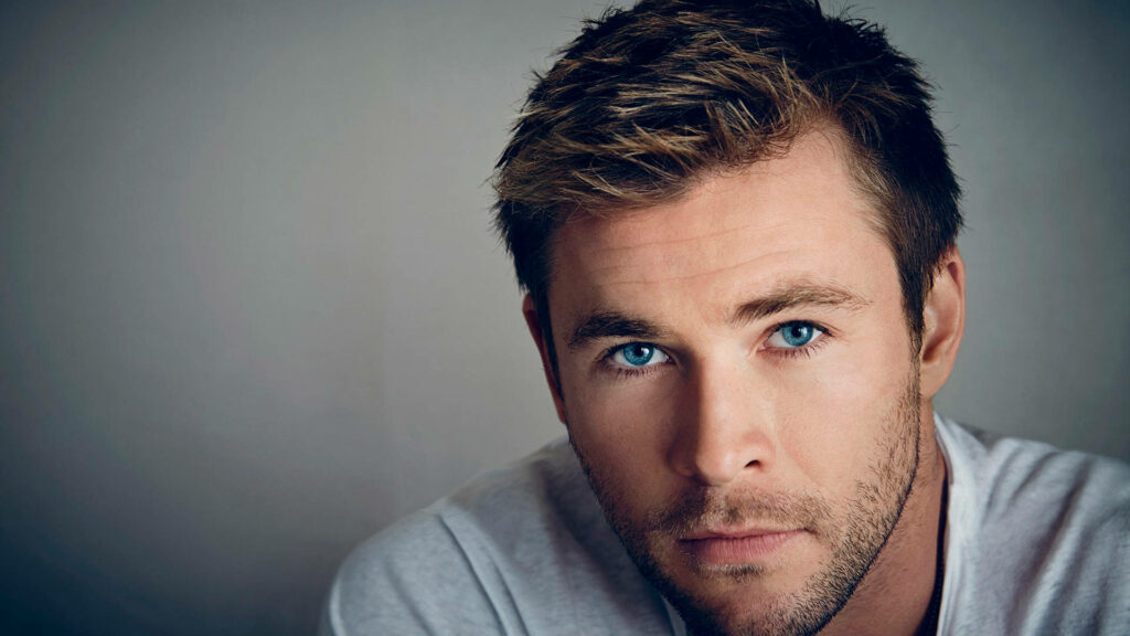 Chris Hemsworth close-up with striking blue eyes against soft neutral wallpaper background