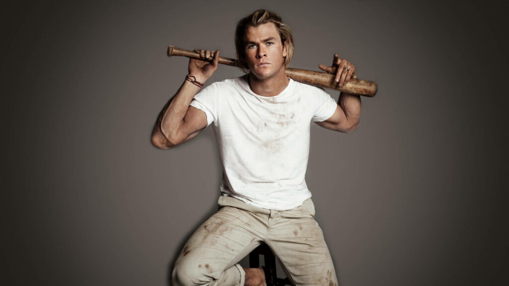 Chris Hemsworth in rugged white outfit holding baseball bat on shoulders against plain background Wallpaper