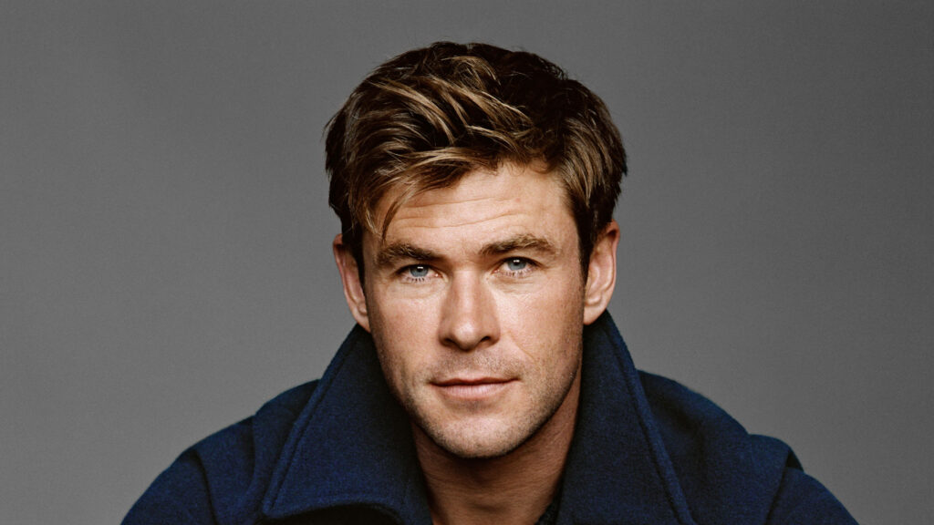 Chris Hemsworth confident in blue jacket posing against simple gray background wallpaper