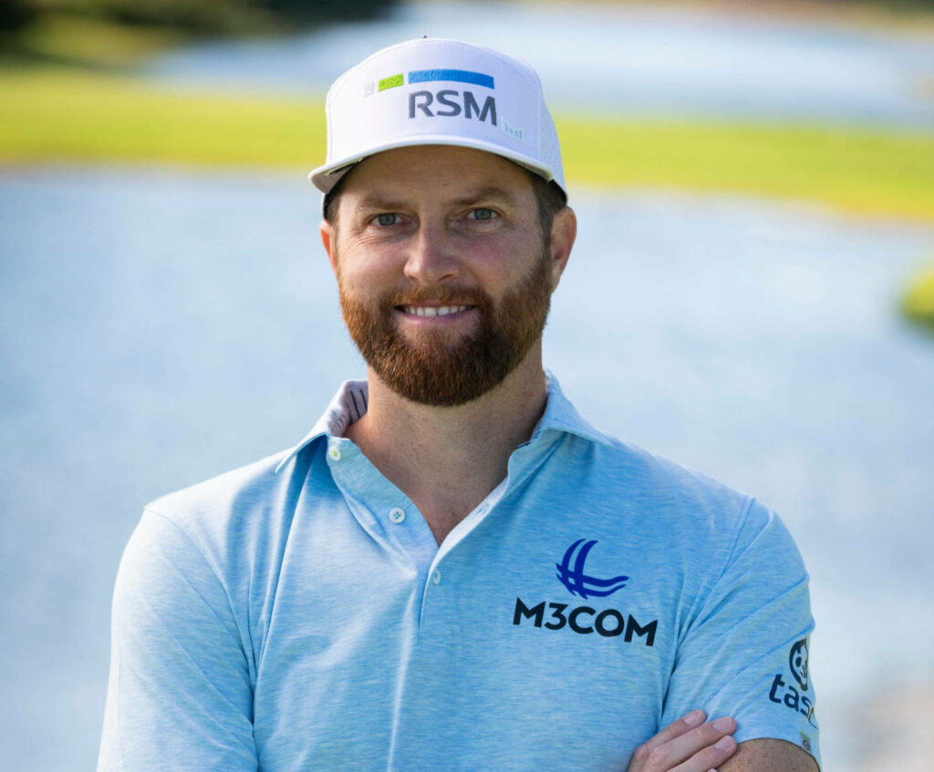 Golfer Chris Kirk in light blue polo and white cap outdoors by serene golf course landscape wallpaper