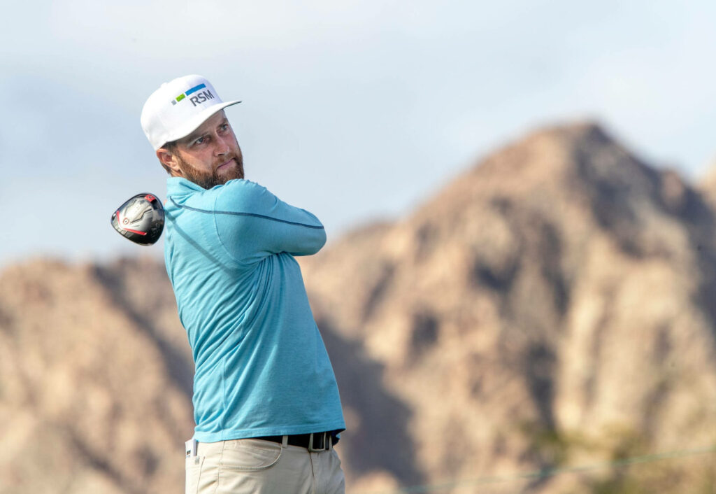 Chris Kirk mid golf swing with focused expression rugged mountain backdrop and blue athletic attire Wallpaper