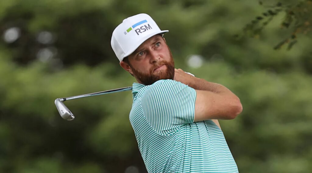 Golfer Chris Kirk mid-swing in striped attire with focused expression on blurred green background Wallpaper