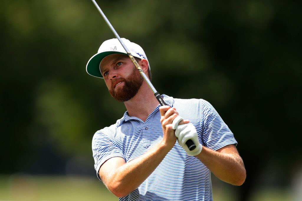 Chris Kirk professional golfer mid swing wearing striped polo and cap on blurred golf course background Wallpaper