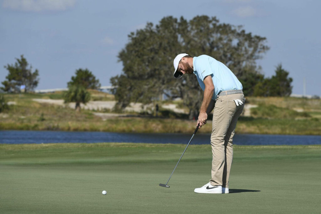 Chris Kirk putting on sunny golf course with blue sky green grass and calm water backdrop Wallpaper